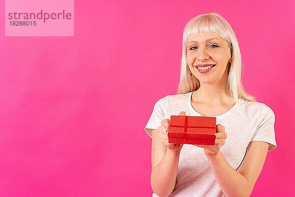 Lächelndes Überreichen eines Geschenks an die Kamera  blondes kaukasisches Mädchen im Studio auf rosa Hintergrund