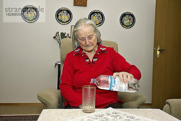 ältere Frau  Seniorin schenkt sich ein Glas Mineralwasser ein  München  Bayern  Deutschland  Europa