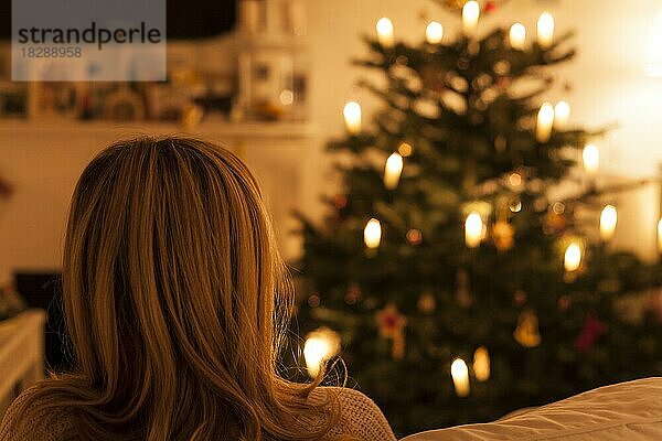 Frau sitzt auf Sofa vor Weihnachtsbaum  Rückenansicht