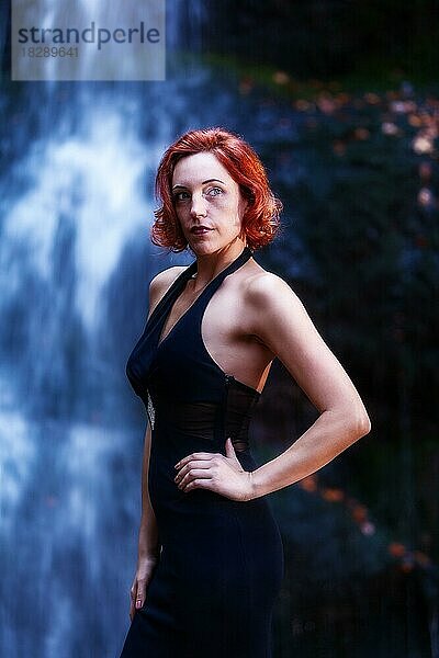 Elegante rothaarige Frau vor einem Wasserfall