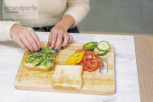 Unbekannte Person  die in der Küche zu Hause ein Gemüsesandwich zubereitet. Platzieren des Rucola