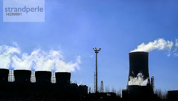 Industriegebiet mit Kühlturm und Schornsteinen als Silhouette vor blauem Himmel am BASF-Chemieproduktionsstandort im Hafen von Antwerpen  Belgien  Europa