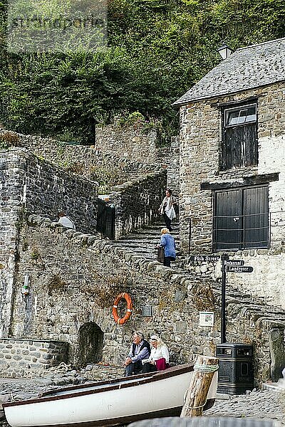 Menschen  die sich ausruhen  und andere  die sich durch die steilen Kopfsteinpflasterstraßen von Clovelly bewegen. Clovelly  Devon  England  UK