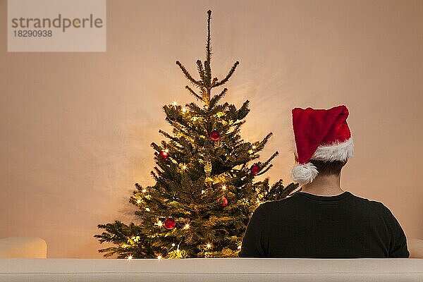 Ein Mann sitzt auf einem Sofa vor einem Weihnachtsbaum