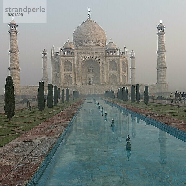 Taj Mahal in der Morgendämmerung eines Januarmorgens  teilweise in den Nebel getaucht. Der klassische Blick auf das Mausoleum  das sich im Wasserkanal des Gartens spiegelt. Weltwunder  UNESCO-Weltkulturerbe  berühmtes Wahrzeichen und Touristenattraktion. Agra  Uttar Pradesh  Indien  Asien