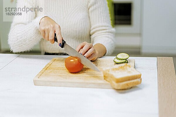 Unbekannte Person  die zu Hause ein Gemüsesandwich zubereitet und Tomatenscheiben schneidet