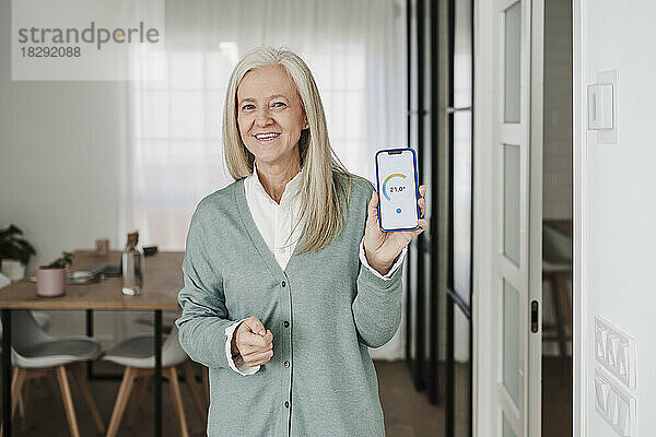 Glückliche Frau zeigt zu Hause die mobile Thermostat-App auf dem Gerätebildschirm