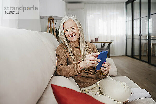 Glückliche reife Frau  die zu Hause mit dem Handy sitzt