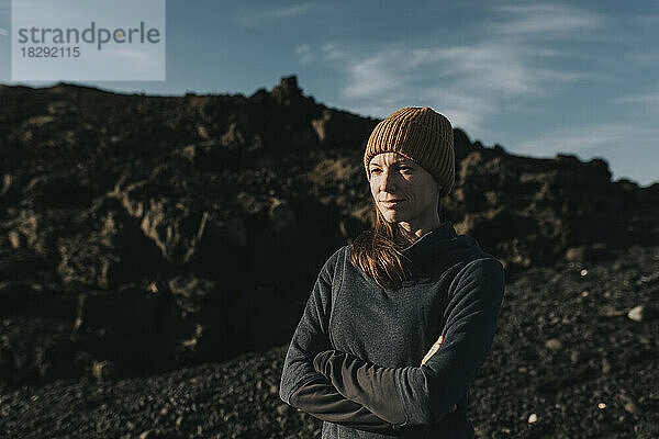 Contemplative woman wearing knit hat standing with arms crossed at Janubio Beach  Lanzarote  Canary Islands  Spain
