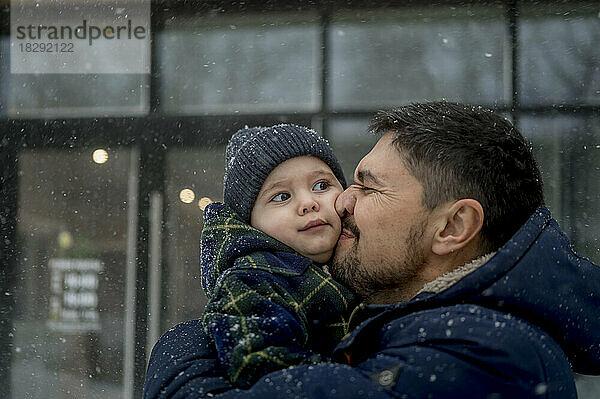 Glücklicher Vater umarmt Sohn im Schneefall