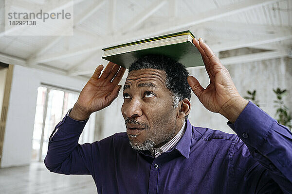 Reifer Mann balanciert Buch auf dem Kopf