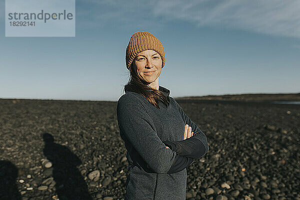 Happy woman wearing knit hat standing with arms crossed at Janubio Beach  Lanzarote  Canary Islands  Spain