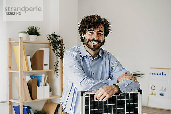 Glücklicher junger Geschäftsmann mit Solarpanel im Büro