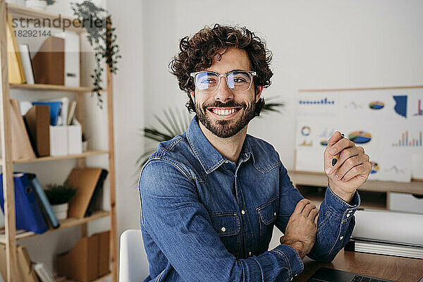 Fröhlicher junger Ingenieur mit Brille und Stift im Büro