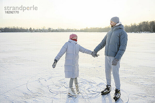Vater hält Händchen seiner Tochter und übt Eislaufen auf dem Wintersee