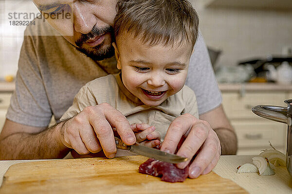 Vater schneidet mit Sohn in der Küche rotes Fleisch