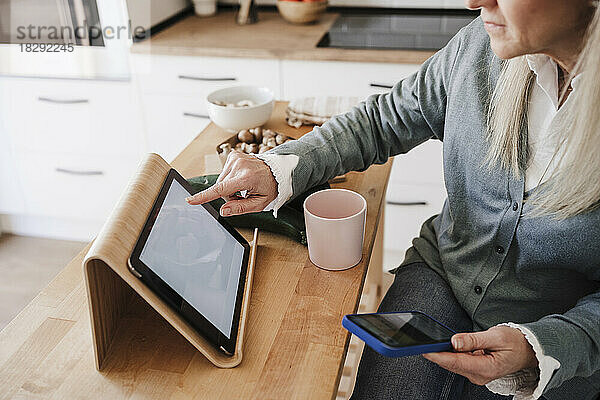 Frau sitzt am Tisch in der Küche und benutzt einen Tablet-PC