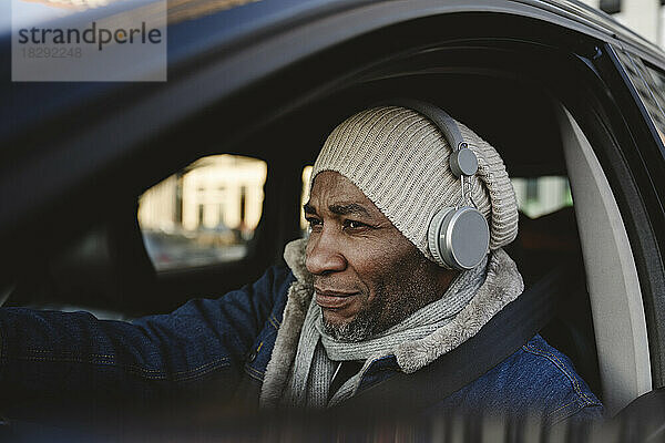 Reifer Mann mit kabellosen Kopfhörern unterwegs im Auto