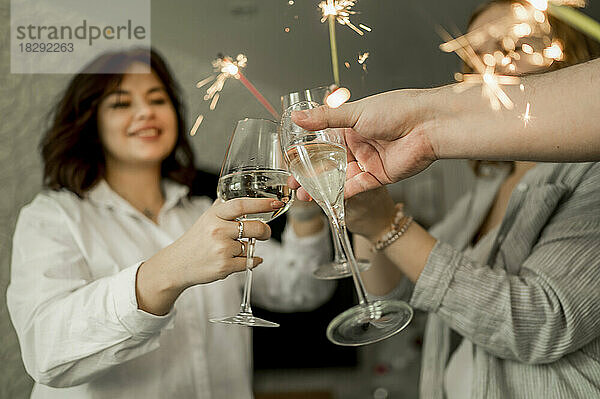 Fröhliche Freunde  die zu Hause ein Glas Champagner und Wunderkerzen genießen