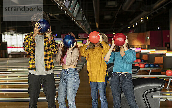 Freunde bedecken ihr Gesicht mit Bällen auf der Bowlingbahn