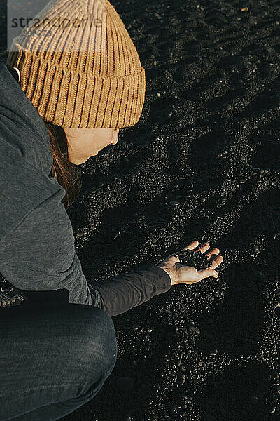 Frau sammelt schwarzen Sand am Vulkanstrand auf