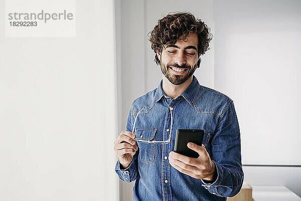 Lächelnder junger Unternehmer  der sein Mobiltelefon im Büro nutzt