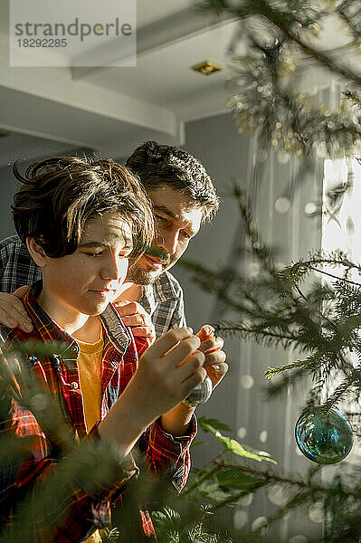 Vater und Sohn schmücken zu Hause den Weihnachtsbaum