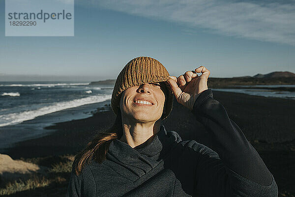 Lächelnde Frau  die durch eine Strickmütze am Strand von Janubio  Lanzarote  Kanarische Inseln  Spanien  späht