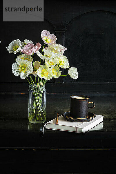 Frische isländische Mohnblumen im Glas neben Kaffeetasse und Tagebuch auf schwarzem Klavier