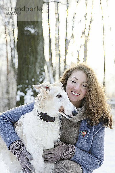 Glückliche reife Frau mit weißem Windhund im Winterpark