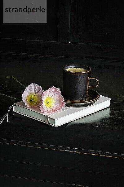 Iceland poppy flowers by coffee cup on diary over black piano
