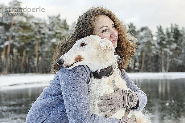 Reife Frau umarmt Windhund vor zugefrorenem See