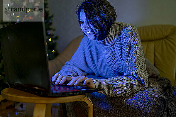 Frau schaut sich abends im Wohnzimmer einen Film auf dem Laptop an