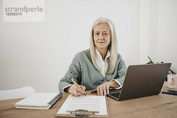 Lächelnder Freiberufler mit Dokumenten und Laptop am Schreibtisch