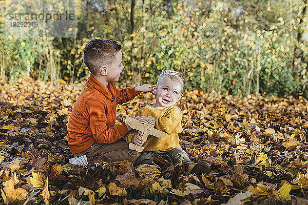 Niedlicher kleiner Junge hält ein Spielzeugflugzeug in der Hand und genießt es mit seinem Bruder auf Herbstblättern