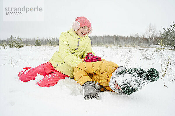 Fröhliches Mädchen  das mit seinem Bruder im Schnee spielt und Spaß hat