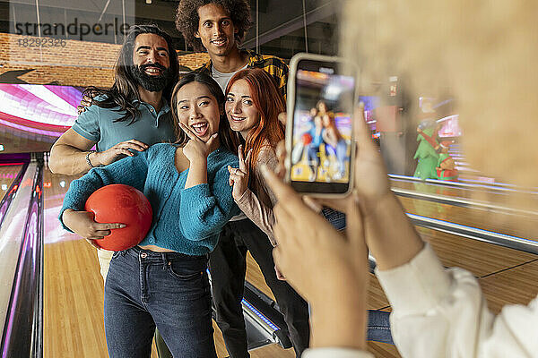 Junge Frau fotografiert Freunde per Handy in der Bowlingbahn