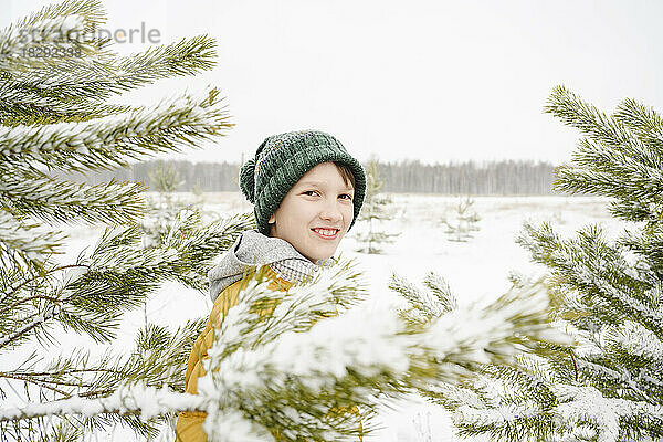 Lächelnder Junge steht inmitten schneebedeckter Kiefern