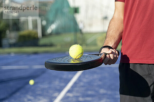 Hand of man holding tennis racket and ball at sports court