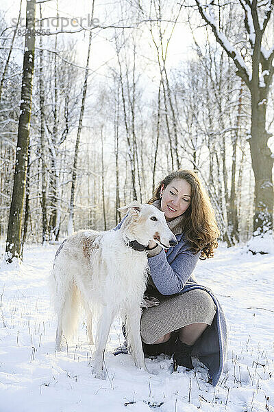 Glückliche reife Frau streichelt Windhund im Winterpark