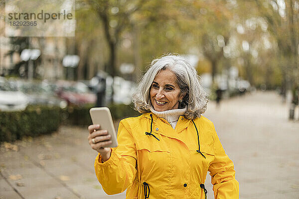 Glückliche Seniorin benutzt Smartphone am Fußweg