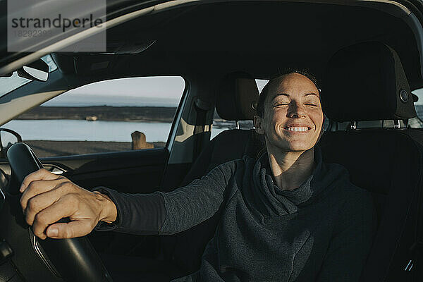 Glückliche Frau mit geschlossenen Augen sitzt im Auto