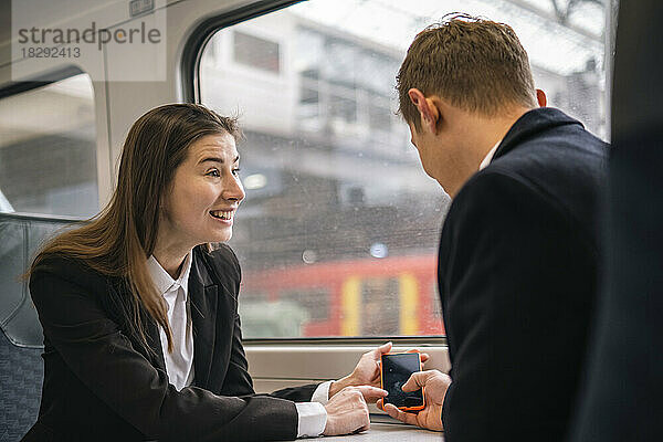 Glückliche Geschäftsfrau teilt Smartphone mit Kollege im Zug