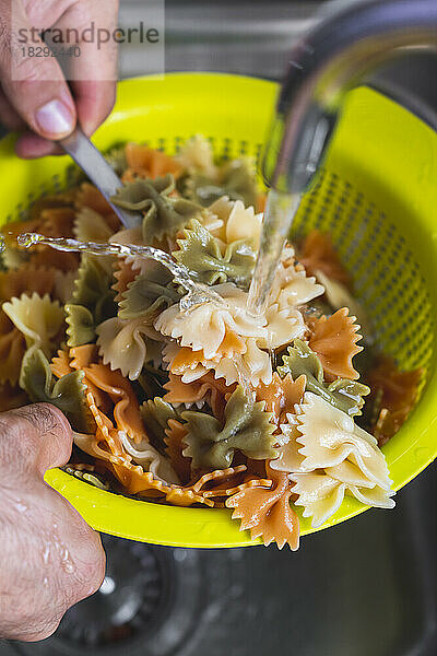 Hands of man washing bow tie pasta in sink