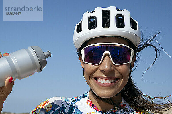Glücklicher Radfahrer mit Wasserflasche unter dem Himmel an einem sonnigen Tag