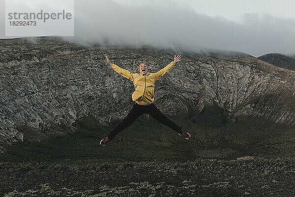 Carefree woman with arms outstretched jumping at Caldera Blanca volcano  Lanzarote  Canary Islands  Spain