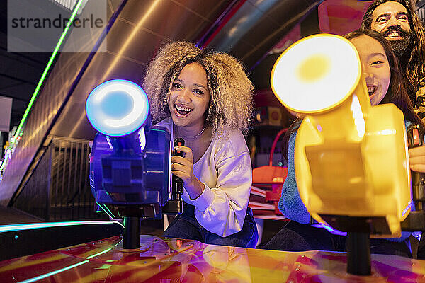 Happy young woman with friends playing video game in amusement arcade