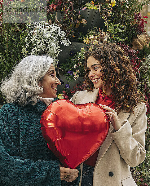 Fröhliche Enkelin und Großmutter halten einen roten herzförmigen Ballon in der Hand