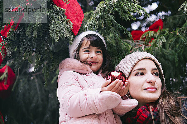 Mutter mit lächelnder Tochter hält Weihnachtskugel