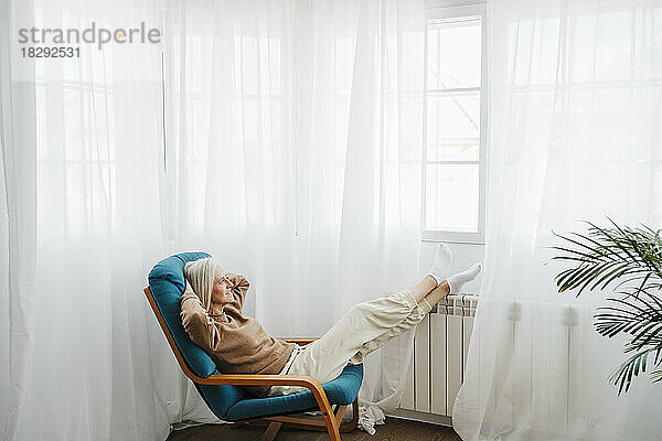 Frau entspannt sich zu Hause auf einem Sessel vor dem Fenster